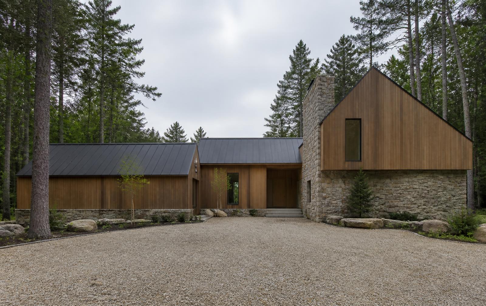 Concept visualization of the land-side entry elevation of a lakeside residence — timber cladding on a fieldstone base under a dark standing-seam gable roof