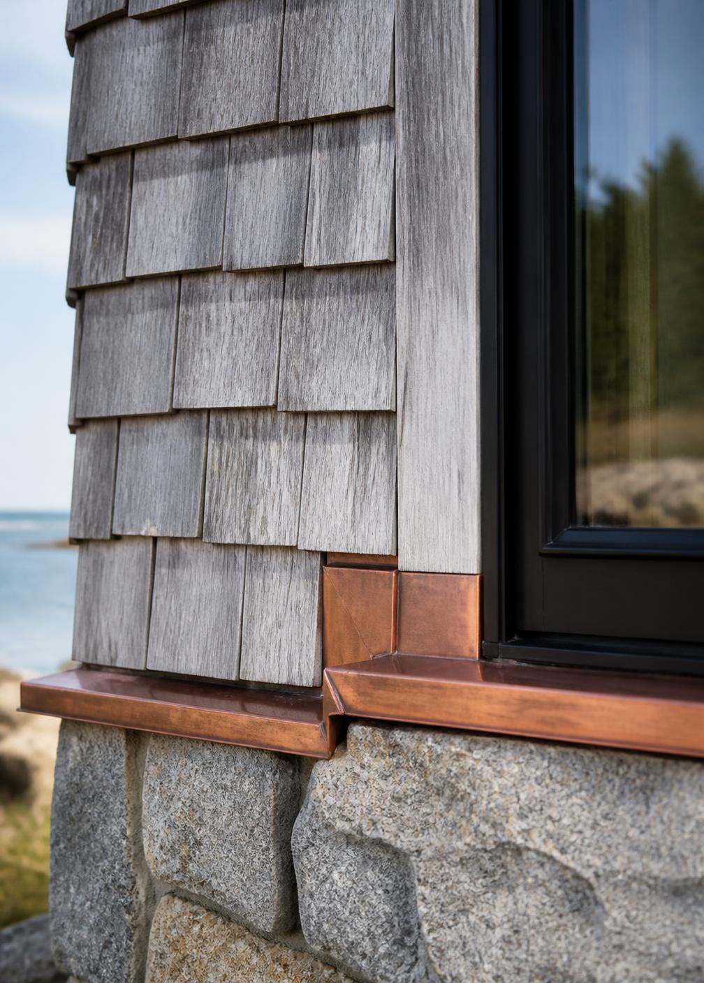 Concept visualization of a detail where weathered cedar shingle meets a granite base with copper flashing and a black window jamb