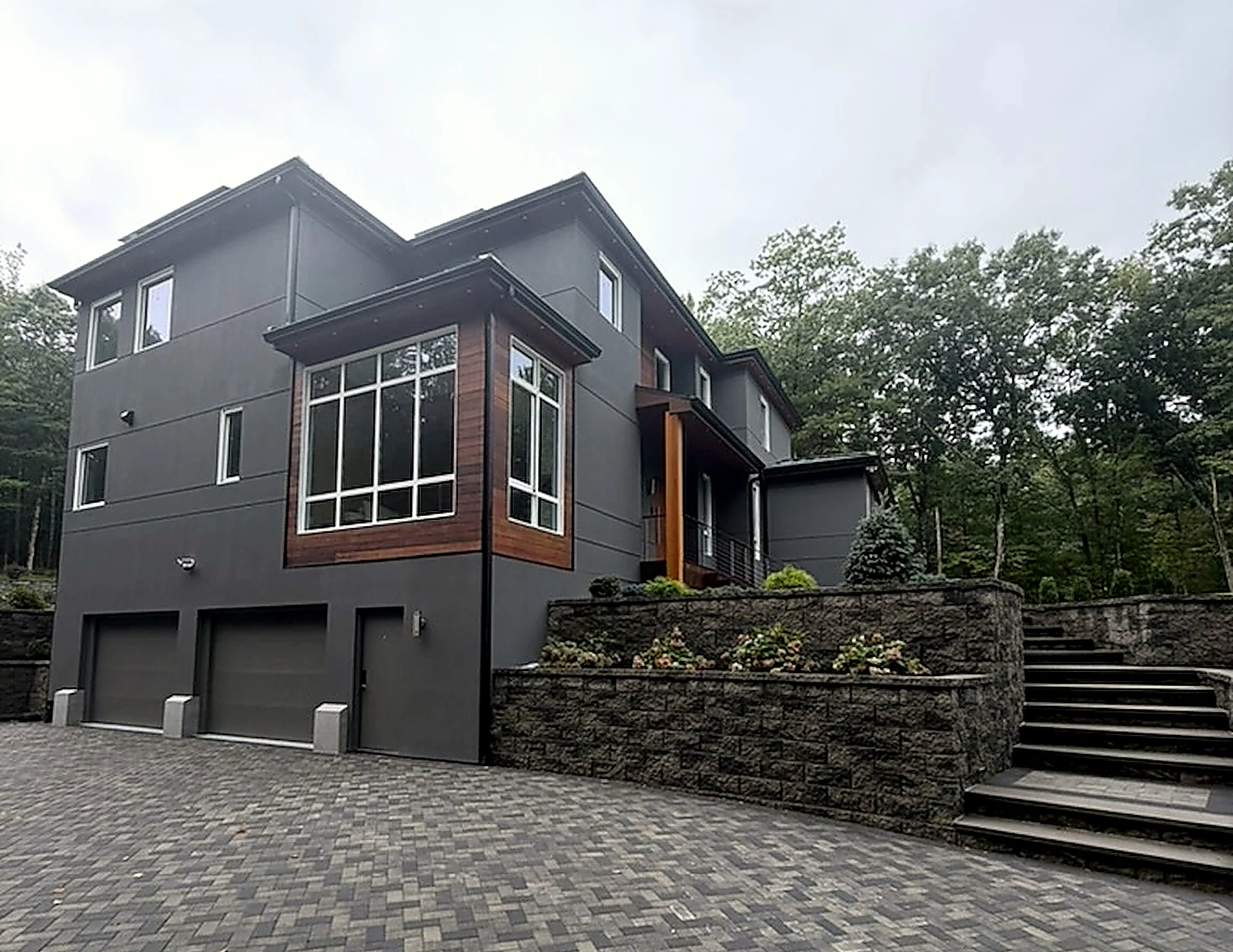 Bedford Residence — side elevation with dark siding, mahogany accent panels and paver drive