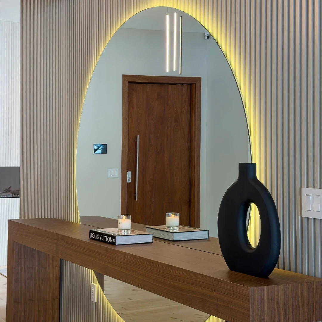 Entry at the Bedford Residence with a walnut console, backlit arched mirror and fluted plaster wall beside the mahogany front door