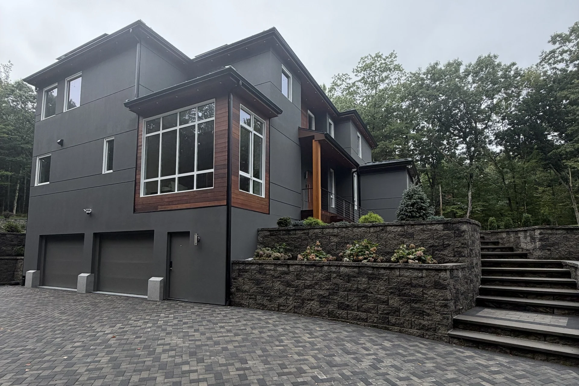 Front elevation of the Bedford Residence with charcoal siding, mahogany accent panels, corner glazing above the garages and a herringbone paver court