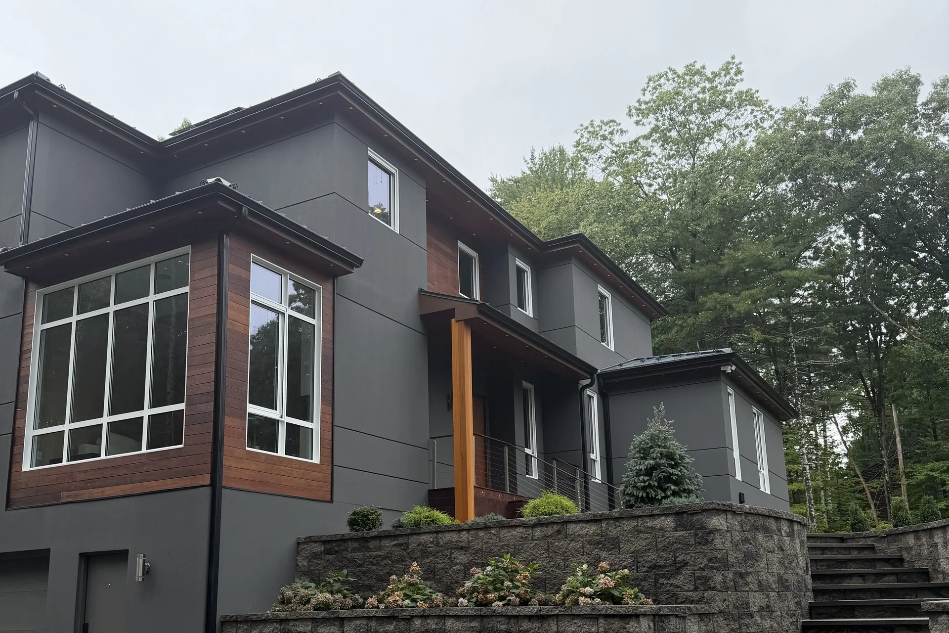 Bedford Residence seen from the paver court, with stacked charcoal volumes, mahogany accent panels and terraced stone retaining walls