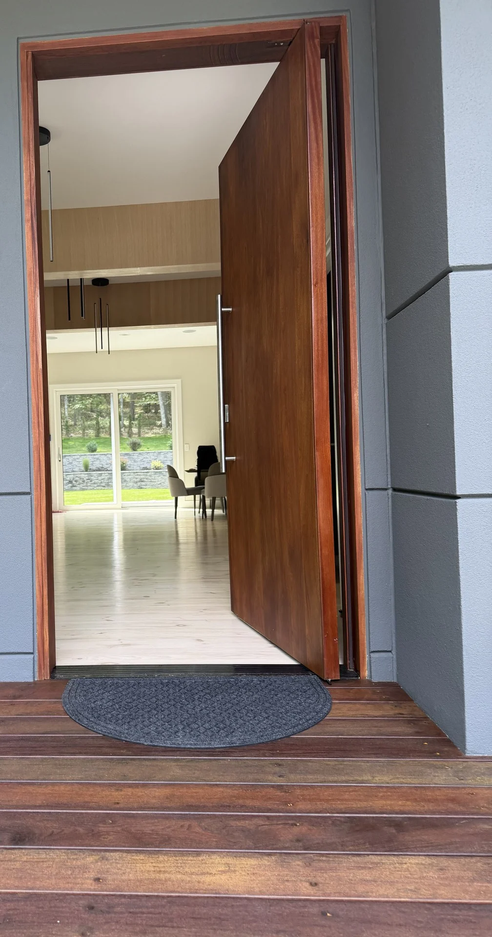 Open mahogany pivot entry door at the Bedford Residence over a mahogany deck, looking through the hall to glazing beyond