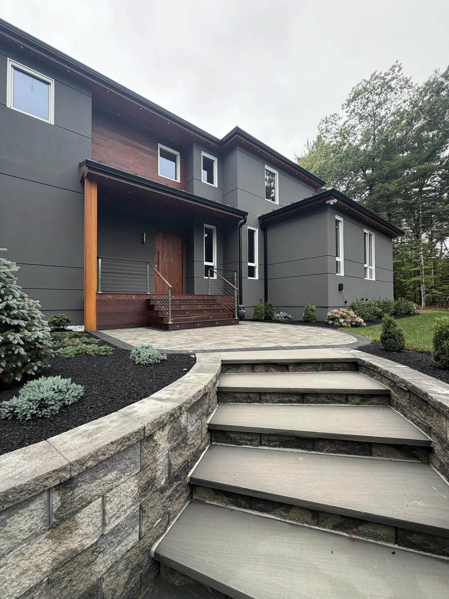 Curved granite entry steps at the Bedford Residence rising through stone retaining walls to the mahogany entry portico