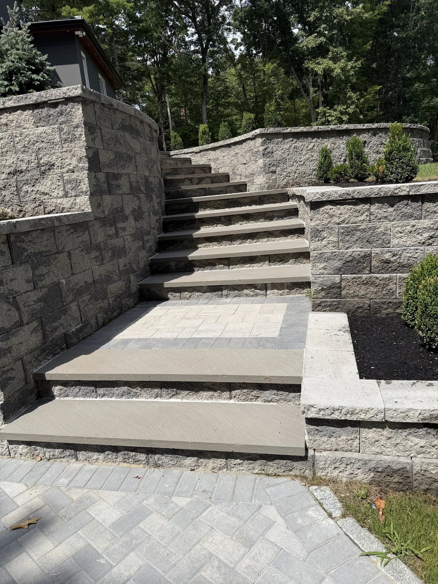 Granite tread stair and stone retaining walls at the Bedford Residence, set into a graded slope beside the paver drive