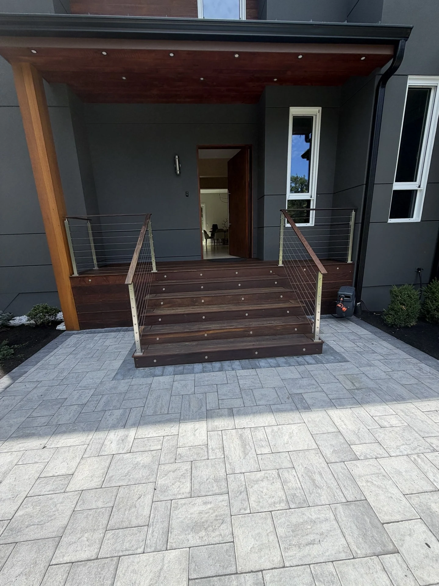 Entry portico at the Bedford Residence with a mahogany soffit and post, cable-rail steps and a large-format paver court