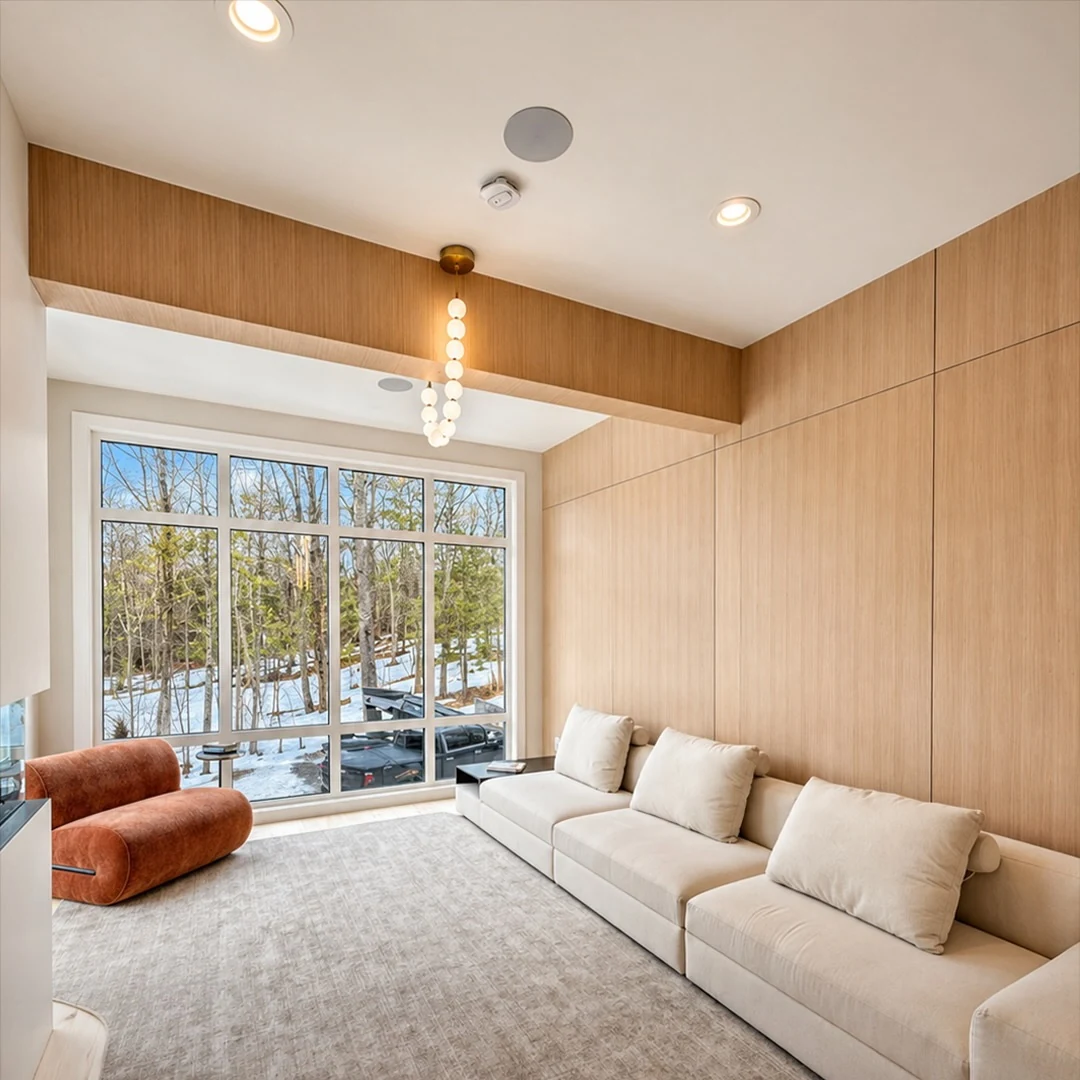 Lounge at the Bedford Residence panelled in white oak with a corner glass wall looking onto snow and woodland