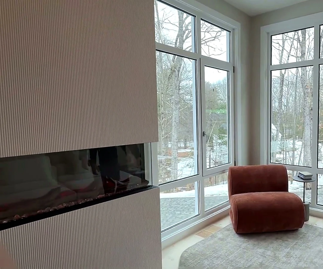 Fireplace wall at the Bedford Residence in vertical fluted plaster with a linear burner, flanked by corner glazing and a terracotta lounge chair