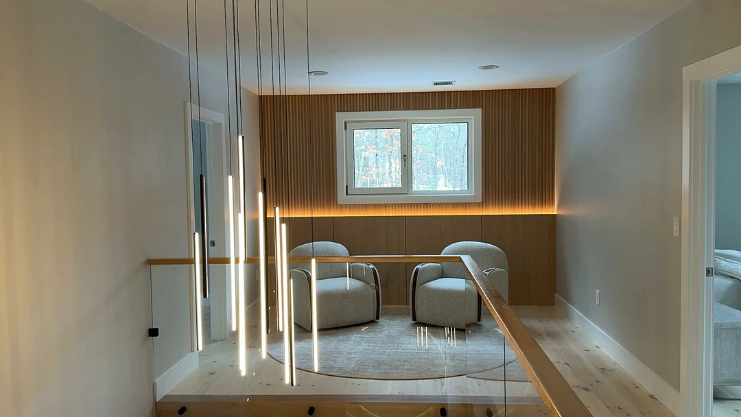 Upper landing at the Bedford Residence with a cluster of linear pendants, glass balustrade and a slatted walnut feature wall with concealed lighting